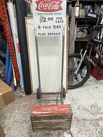 Front view of the vintage Coca-Cola dolly featuring the large metal advertising sign and wooden crate base.