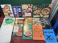 Photo showing eleven vintage cookbooks with colorful covers and some wear.