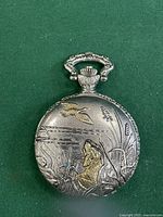 Front cover of the vintage pocket watch showing detailed engraving of a dog and a flying duck with golden accents; ornate winding crown visible.