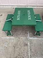 Green portable picnic table with two attached benches, branded with white 'BOTA BOX' text, fully opened and standing on concrete.