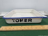 Side view of large vintage toner pan with ruler showing approximately 11 inch width, white with blue rim and black 'TONER' lettering.