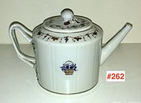 Front quarter view showing spout, handle, floral basket motif on body, lid with bud finial.