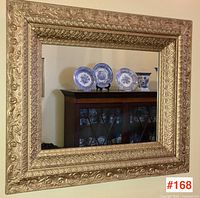 Full view of rectangular mirror with ornate gilt frame hanging on wall, reflects cabinet and blue-and-white china.