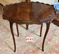 Full view of the antique mahogany tray table showing scalloped wood top, brass handles, and cabriole legs on a patterned carpet.