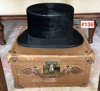 Black top hat on closed leather box with brass latch and leather handle