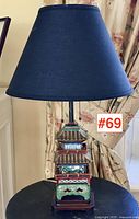 Full view of pagoda table lamp with dark blue shade on black tabletop against floral curtains