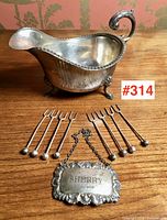 Overview of lot: gravy boat, decanter label, eight cocktail picks on wooden surface