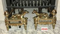 Pair of brass antique andirons positioned before fireplace on marble hearth.