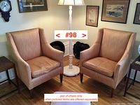 Two upholstered armchairs shown side by side in room next to lamp and wall decor.