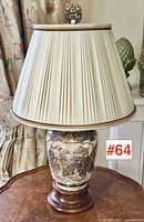 Full view of the satsuma pottery table lamp on a wooden table, with cream pleated lampshade and carved finial