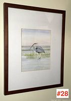 Entire framed watercolor painting with white mat and brown wooden frame hung on wall