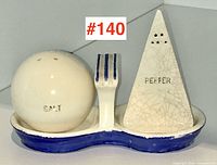 Front view of ceramic salt and pepper shaker set modeled after 1939 New York World's Fair symbols; spherical salt and triangular pepper shakers on blue and white tray with fork-shaped divider.