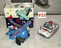 Both tin toys shown together: blue training plane with box alongside white racing car with Martini and Shell logos.
