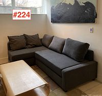 Left-front view of gray L-shaped sofa bed with back cushions and coffee table in foreground