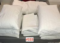 Photo showing stacked white pillows, folded bedding including mattress covers and a feather duvet.