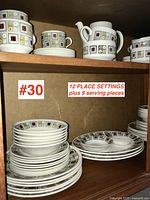 Wooden cabinet shelf displaying portions of the set including plates, bowls, cups and saucers