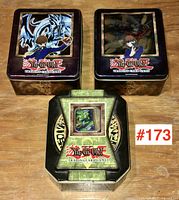 Three Yu-Gi-Oh collectible metal tins displayed, two with character and dragon artwork, one with embossed design.