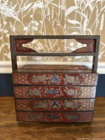 Front view of the antique lacquer box showing three stacked compartments with floral and geometric inlays and carved handle.