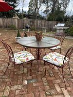 Full view of patio table with four chairs on brick patio. Cushions have colorful bird print. Photo shows outdoor setting.