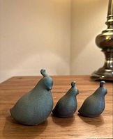 Three raku pottery quail figurines displayed on wood surface with metallic lamp in background
