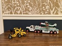 2002 Hess gasoline truck carrying a green and white biplane and three yellow construction toy vehicles on a wooden table