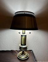 Full view of vintage brass bouillotte laboratory table lamp turned on, showing light glow and shade details.