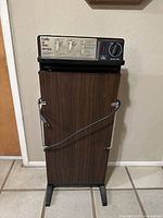 Full view of vintage electric trouser press with wood grain front and black plastic top control panel