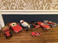Photo showing seven vintage diecast model classic cars and a diecast truck lined up on a wooden surface, various classic designs and colors visible.