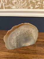 Polished cross-section of the agate slice showing translucent areas, banding, and crystalline texture, displayed upright on a wooden surface.