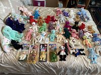 Collection of over 30 assorted Ty Beanie Babies in multiple colors and animal types arranged on a bed showing original tags attached on each.