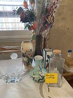 Group photo showing various vases, a glass container with cork, floral arrangements, and a crystal container with a white rose inside.