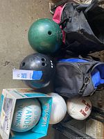 Overview photo showing two bowling balls (green and black), two bowling bags (pink and blue), and a box containing a volleyball and basketball.