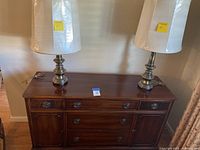 Full view of brown wooden buffet with 5 drawers and 2 brass lamps on top