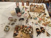 Wide shot of the full collection displayed on a lace tablecloth, showing a variety of small figurines, animals, bears, dolls, and floral pieces arranged across multiple trays and individually