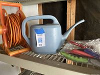 Orange garden hose on reel, blue plastic watering can, and small garden hand tools in bag