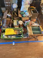 Photo of table covered with various craft supplies, boxed and loose items, with a foldable wooden chair beside the table.