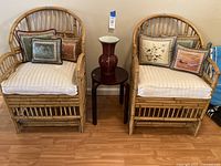 View of the set showing two bamboo chairs each with cushions, small wooden round table, and red vase