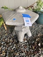 Gray resin pagoda-shaped garden lantern showing top and one side with minor wear, placed on gravel outdoors.