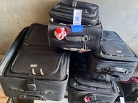 Three stacked black fabric suitcases in large, medium, and small sizes showing exterior views including front zipper pockets and wheels.