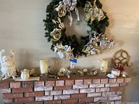 Holiday wreath hanging above a mantel decorated with candles and figurines, showing the wreath's gold and silver accents and angel figure.