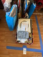 Overview of the lot showing a box with assorted picture frames and paper items alongside blue and multicolored gift bags