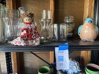 Shelf with clear glass vases, fabric doll figurine in red dress, ceramic bird figurine, and Yankee Candle jar candle.