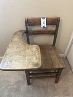 Front view of old wooden school desk showing chair with ladder-back and attached curved writing surface with signs of wear.