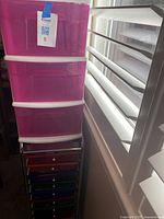 Pink translucent plastic drawer organizer with four drawers stacked vertically, white supports, with a label on the top drawer.