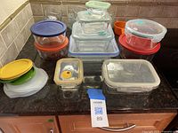Photo showing an assortment of various Pyrex glass and plastic storage containers with colorful sealable lids in red, blue, green, yellow, white, and orange. Containers are of different shapes and sizes, including square, rectangular, and round.