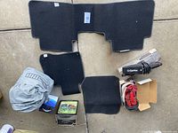 Four black Honda-branded carpet floor mats laid out flat on concrete with additional vacuum cleaner parts, a folded car cover, and boxed items visible around them.