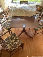 Top view of wooden dining table surrounded by six chairs with patterned seat cushions, showing the table's smooth polished surface with a partly covered lace cloth.