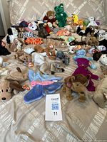 Wide view of a large assortment of TY Beanie Babies plush toys laid out on a bed showing a variety of animals and colors, with original tags.