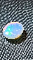 Close-up photo of an oval Ethiopian opal gemstone showing internal blue and green flashes and spotted pattern.