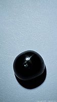 Close-up image of natural black star diopside gemstone showing polished spherical form and the star effect under lighting.